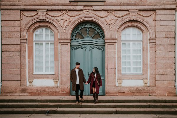 couple holding hands in front of ornate historic building with green door and arched windows in colmar