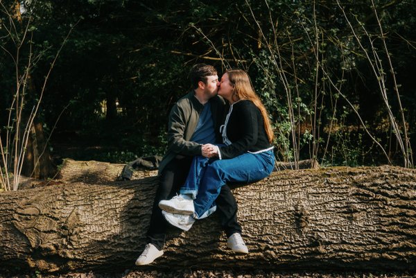 couple kissing on a fallen log surrounded by dense green trees in dappled sunlight