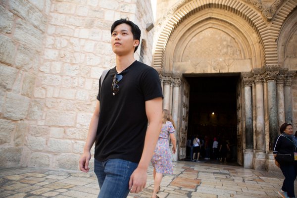 Solo traveler at ornate arched entrance of historic Jerusalem stone building during daytime