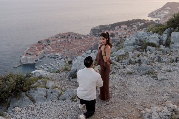 Couple on rocky clifftop overlooking Dubrovnik's terracotta rooftops and Adriatic Sea at golden hour