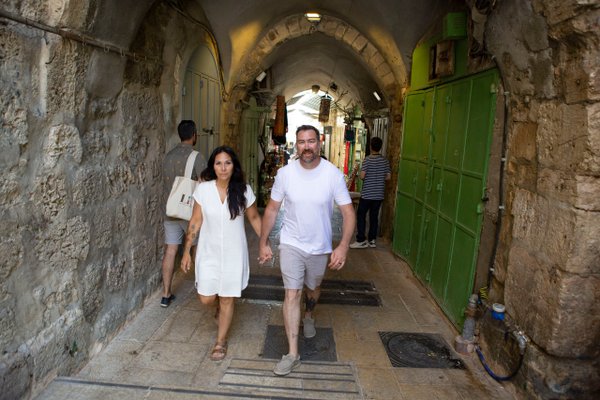 couple walking through narrow arched stone alley with green doors in historic jerusalem old city