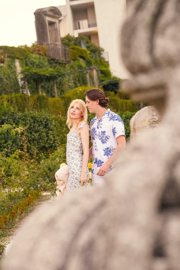 Couple posing in lush garden with ivy-covered walls and stone sculptures at golden hour