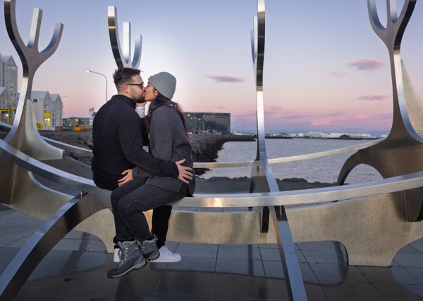 Couple kissing on the Sun Voyager sculpture at dusk with Reykjavík harbor and city lights in the background