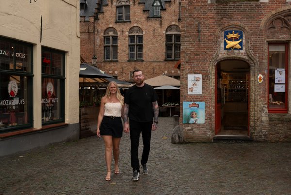 Couple walking hand in hand on cobblestone street lined with historic red brick buildings in Bruges