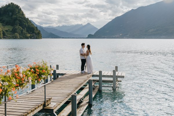 Couple on wooden dock at Lake Brienz with alpine mountains and cloudy sky, Interlaken