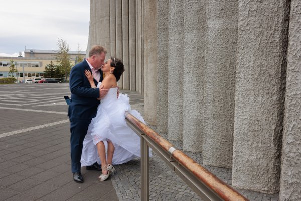 Couple kissing by concrete columns at Hallgrímskirkja, bride in white dress and groom in navy suit