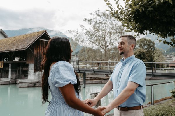 Couple holding hands by a turquoise river and wooden boathouse with mountains in the background