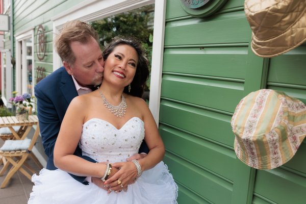 Couple in formal attire posing against a bright green door in daylight, woman in white wedding dress smiling