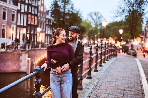 Couple smiling on a canal bridge at dusk, historic buildings and golden streetlights lining the waterway