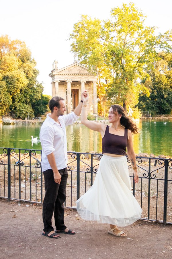 Couple dancing by the Tiber River with a neoclassical temple and golden autumn trees in soft daylight