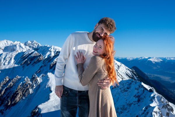 Couple embracing on snowy alpine ridge under clear blue sky, Innsbruck mountains behind
