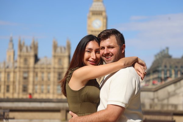 Couple embracing by the Thames with Big Ben and Palace of Westminster in background, London daytime