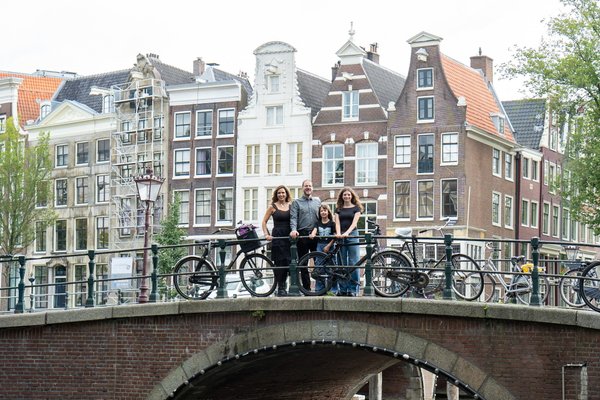 Group of four on a canal bridge with bicycles, historic Dutch townhouses and waterway behind them during daytime