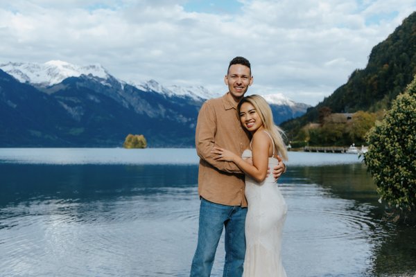 Couple posing by Lake Brienz with snow-capped mountains and forested slopes under cloudy skies