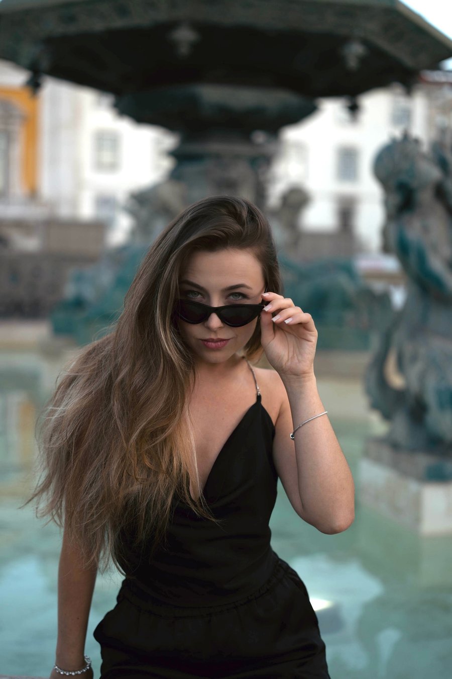 Solo woman in sunglasses posing in Cascais old town square with historic buildings and gateway behind her