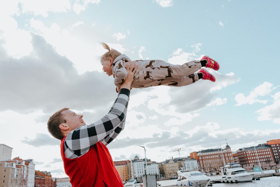 Father lifting young child above his head with Helsinki waterfront and colorful buildings behind them