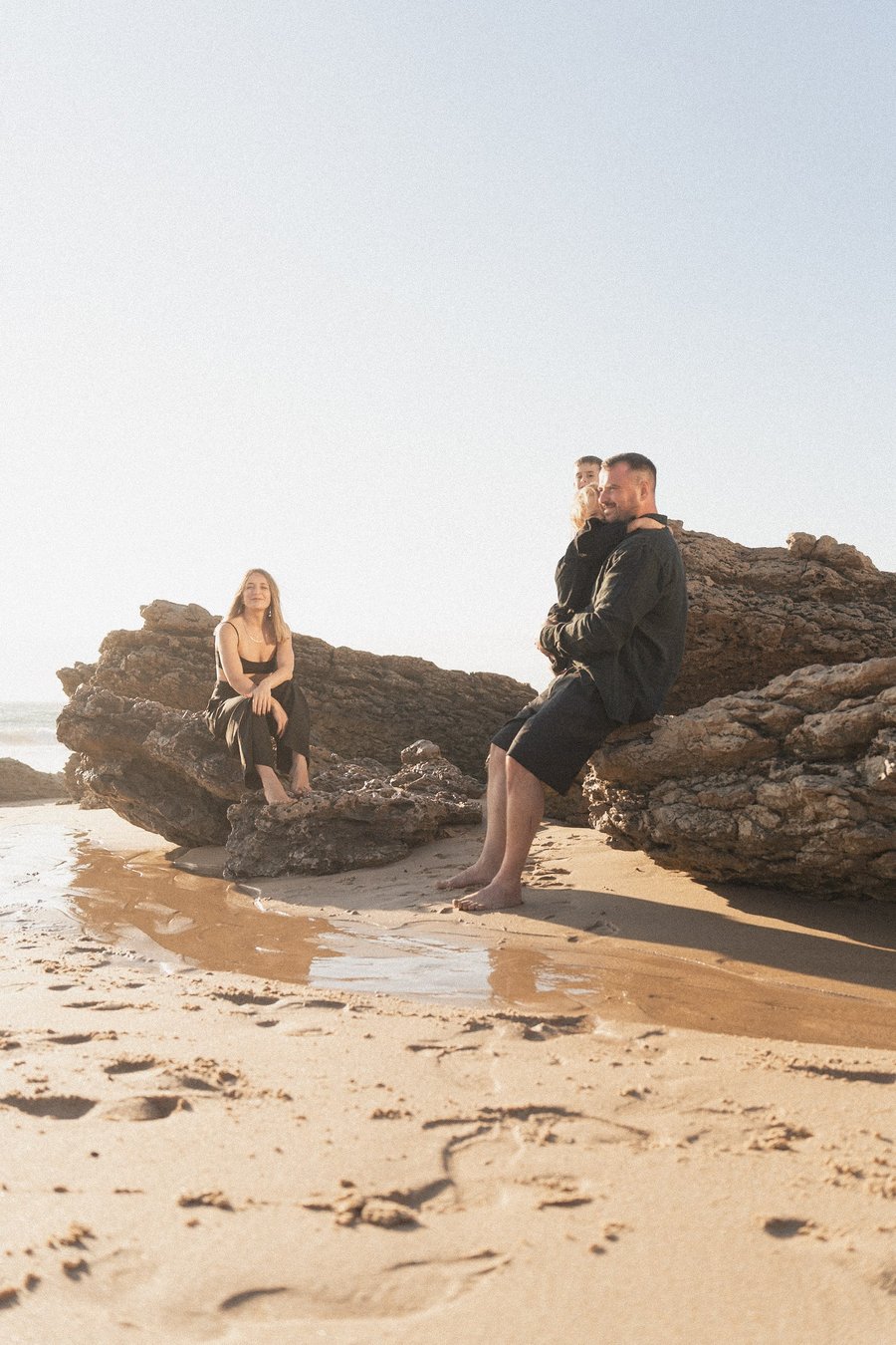 family with child on rocky beach at cascais, golden hour light