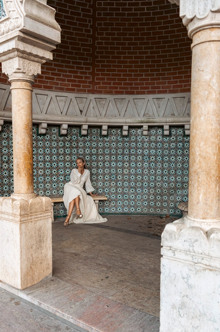 Woman in white dress sitting among ornate columns and turquoise tilework in historic Moroccan-style courtyard
