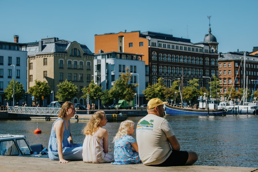 Family of four sitting on dock overlooking colorful waterfront buildings and boats in Helsinki