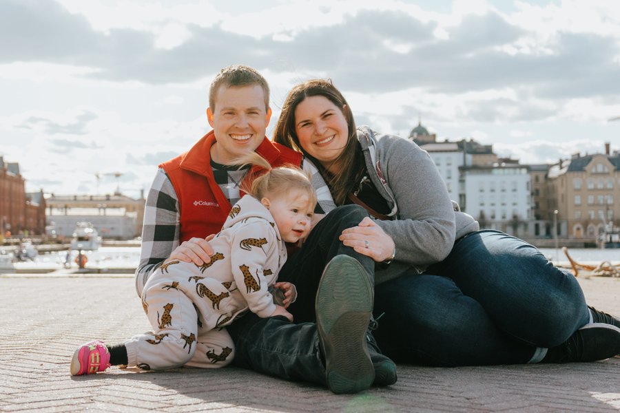 Family with toddler sitting on Helsinki waterfront promenade, cloudy daytime, city buildings in background