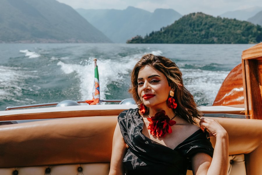 Woman in red earrings on a boat on Lake Como with forested mountains and waves in the background