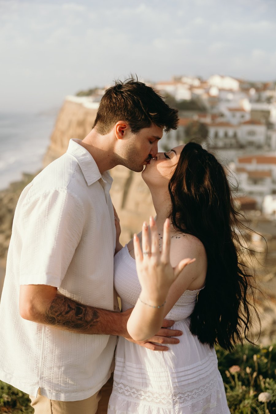 Couple kissing overlooking white-washed cliffside village of Cascais in golden afternoon light