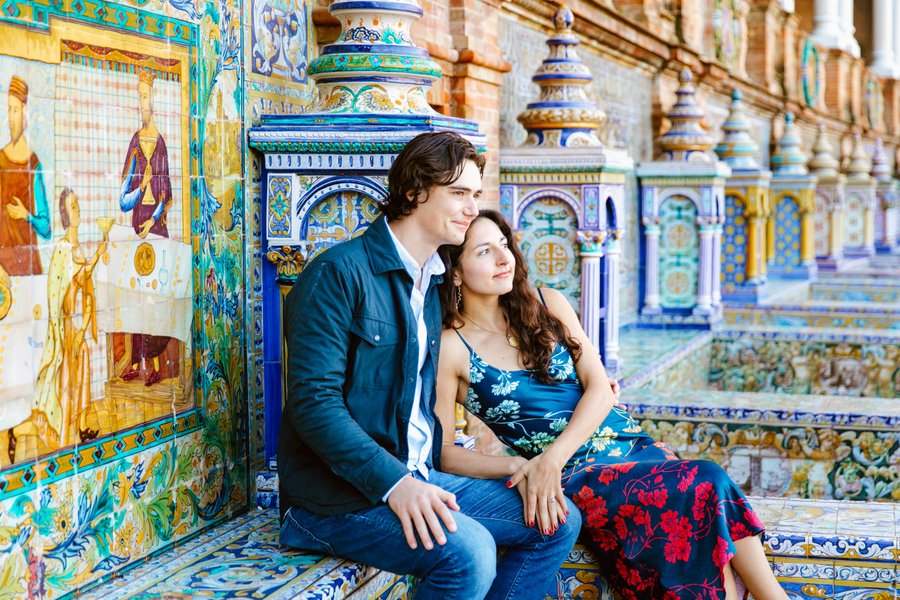 Couple posing together amid ornate blue and yellow tilework in a historic Spanish plaza during daytime