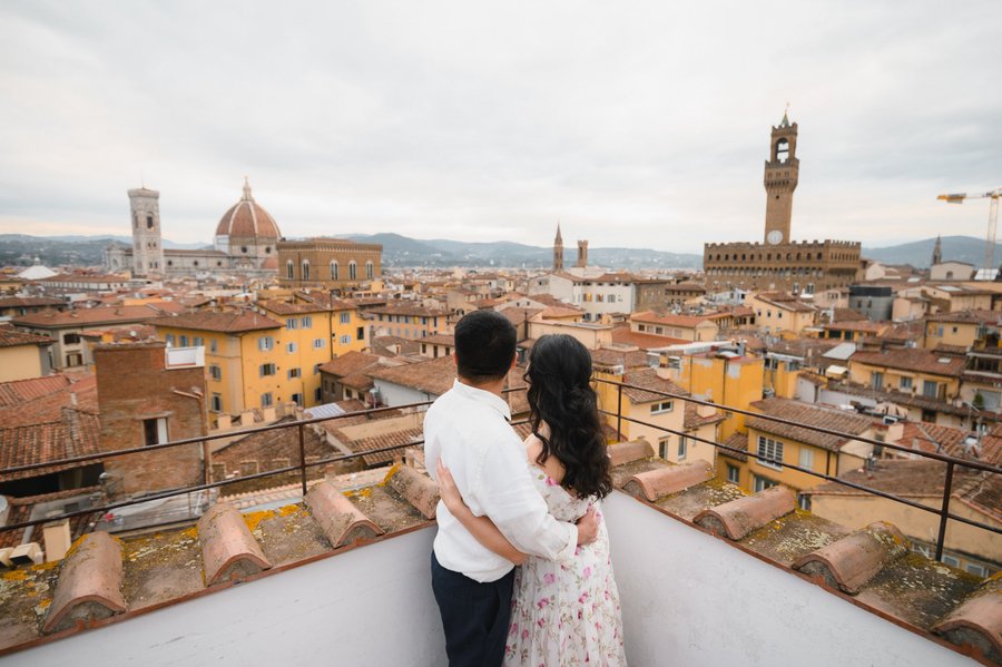 Couple embracing on rooftop overlooking Florence's terracotta skyline and iconic Duomo cathedral under cloudy skies