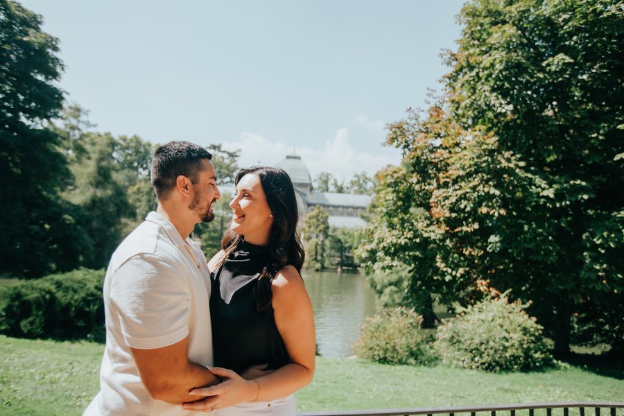 Couple embracing by a riverside garden with ivy-covered walls and a distant bridge in Madrid