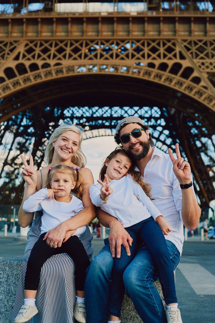 Family of four making peace signs beneath the Eiffel Tower on a bright, sunny day in Paris