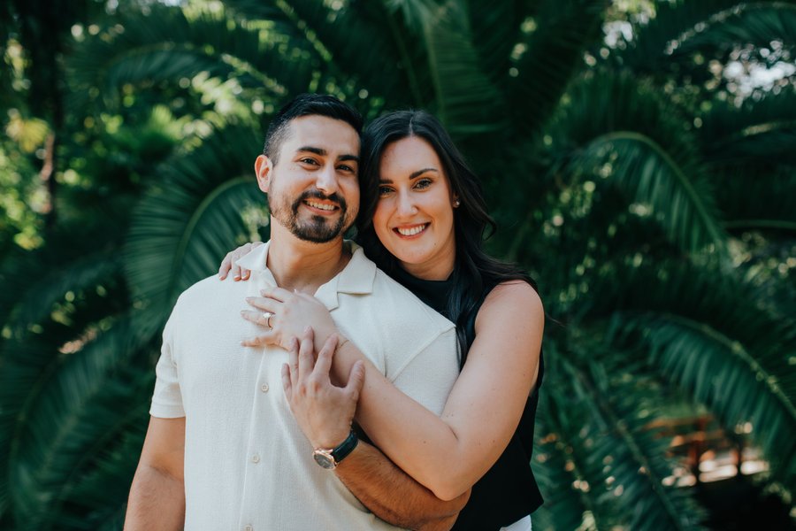 Couple smiling together among lush green foliage in dappled sunlight during daytime