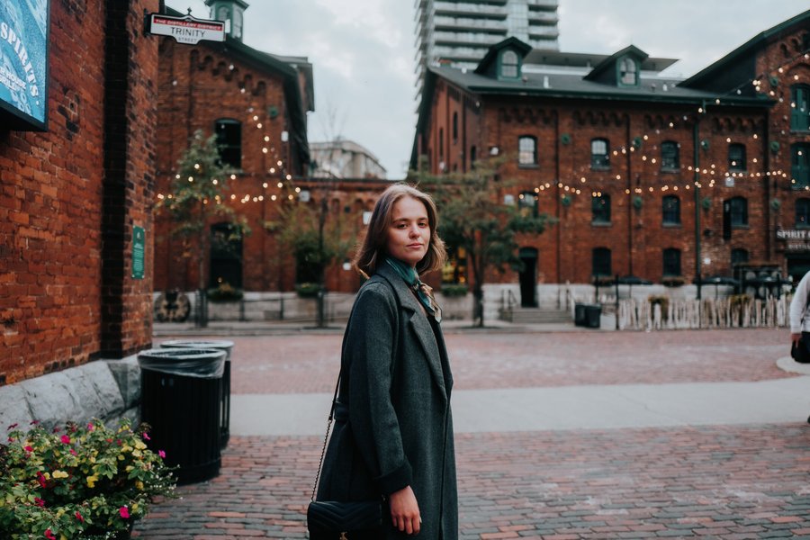 Solo traveler in dark coat at festive Distillery District, surrounded by red brick buildings and holiday lights