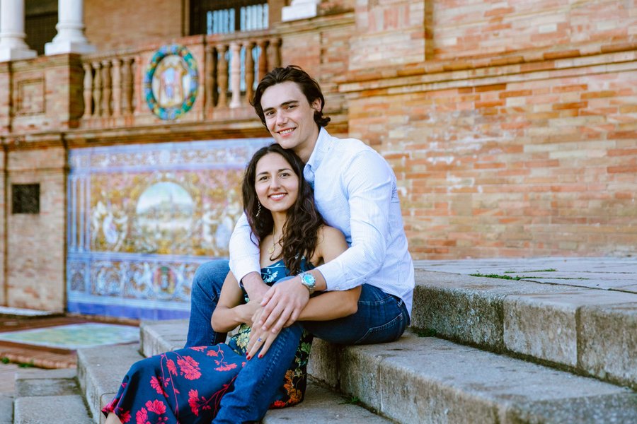 Couple seated on steps against colorful blue tiled brick building facade in daylight