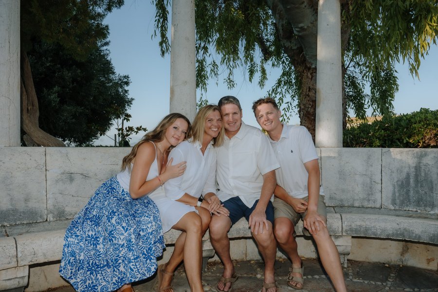 Group of four smiling at Spianada Square in Corfu under tall columns on a sunny day