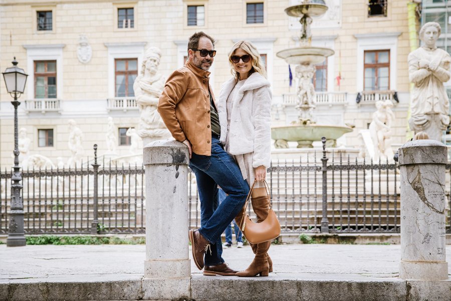 Couple posing at Fontana Pretoria in Palermo, with ornate palazzo and marble statues in background