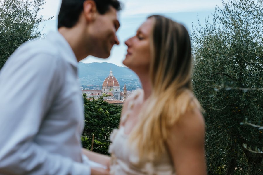 Couple framed by olive trees with Florence's Duomo cathedral glowing in bright daylight behind them