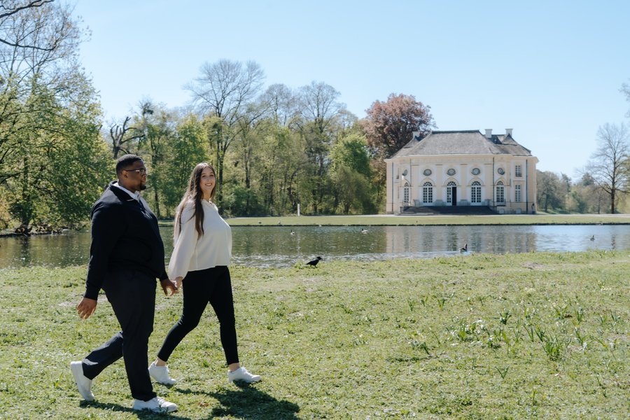 Couple walking by a lake with a pink neoclassical palace reflected in water on a sunny spring day