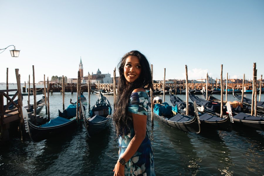 Solo woman posing at Venice's Punta della Dogana with moored gondolas and basilicas in bright daylight
