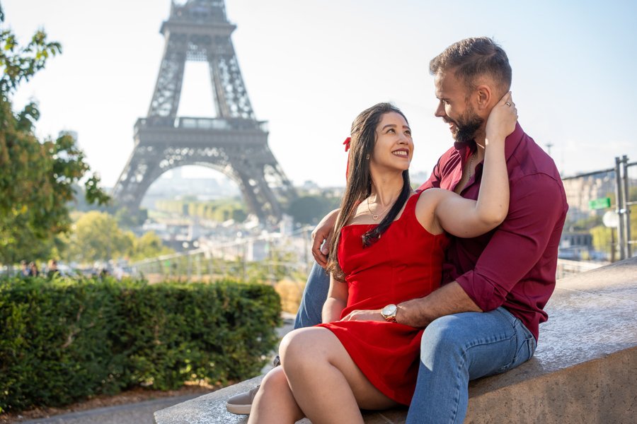 Couple in red and burgundy clothing sitting together overlooking the Eiffel Tower on a sunny day in Paris