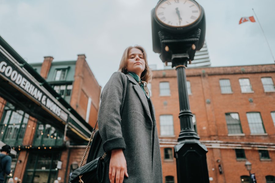 Solo traveler posing beneath vintage street clock in historic brick district during overcast daytime