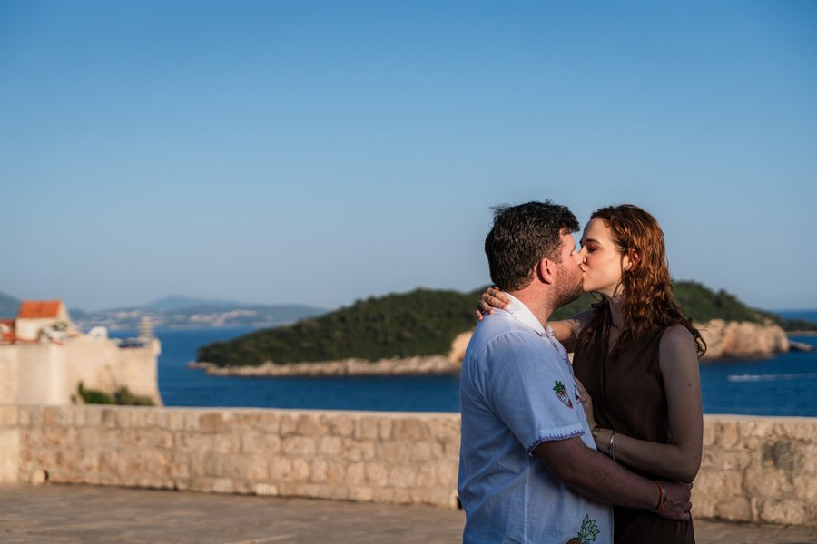 Couple kissing on Dubrovnik city walls overlooking turquoise Adriatic waters and forested islands in clear daylight