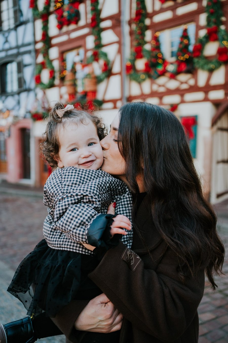 Mother and toddler smiling at festive holiday decorations on a historic half-timbered building in Colmar