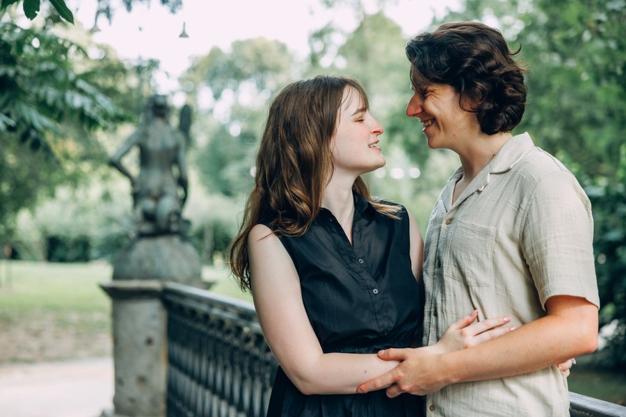 Couple smiling at each other in a lush green park with statues and trees in soft daylight