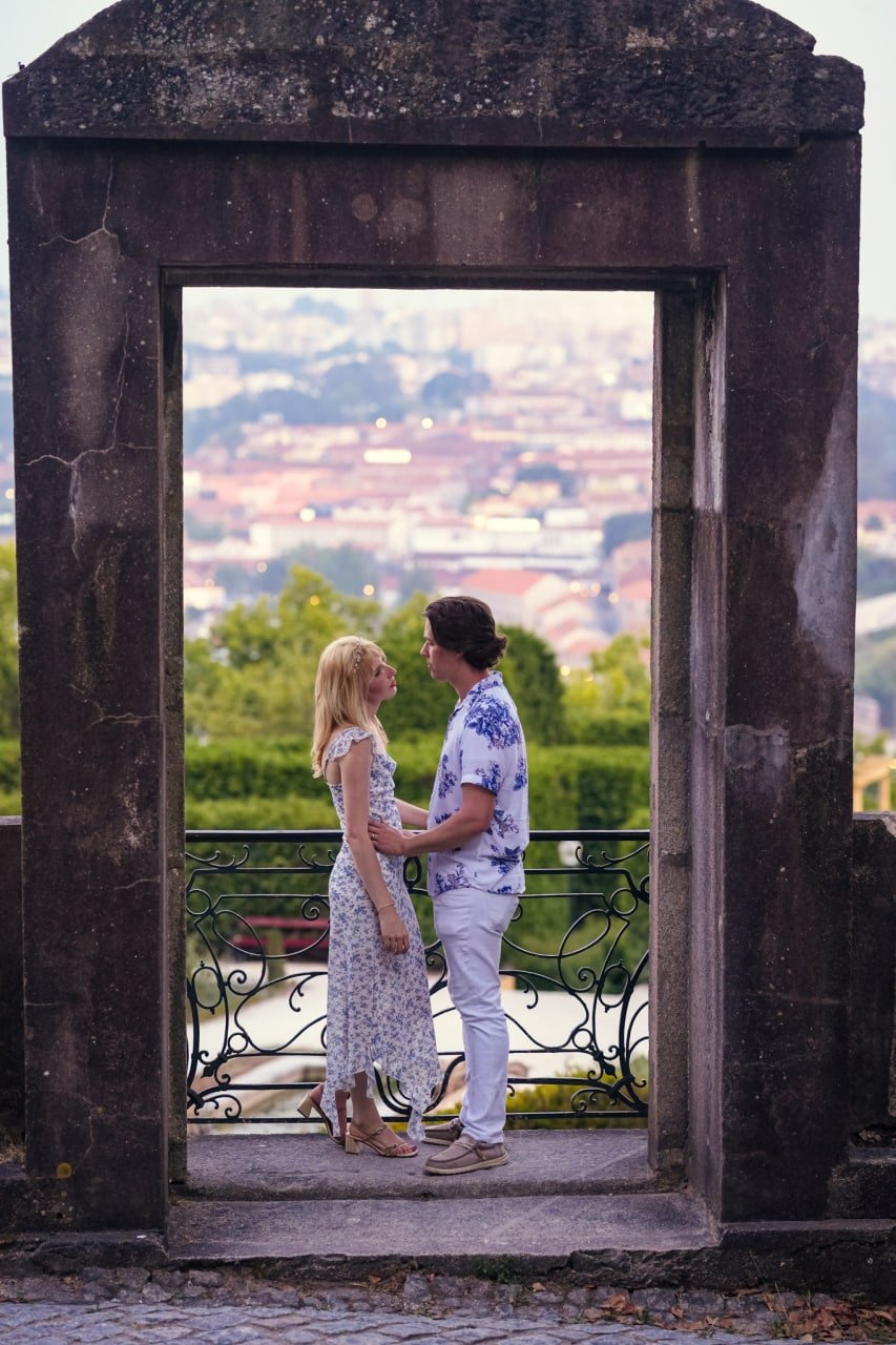 Couple framed by an ancient stone archway gazing at each other, with Porto cityscape blurred in background