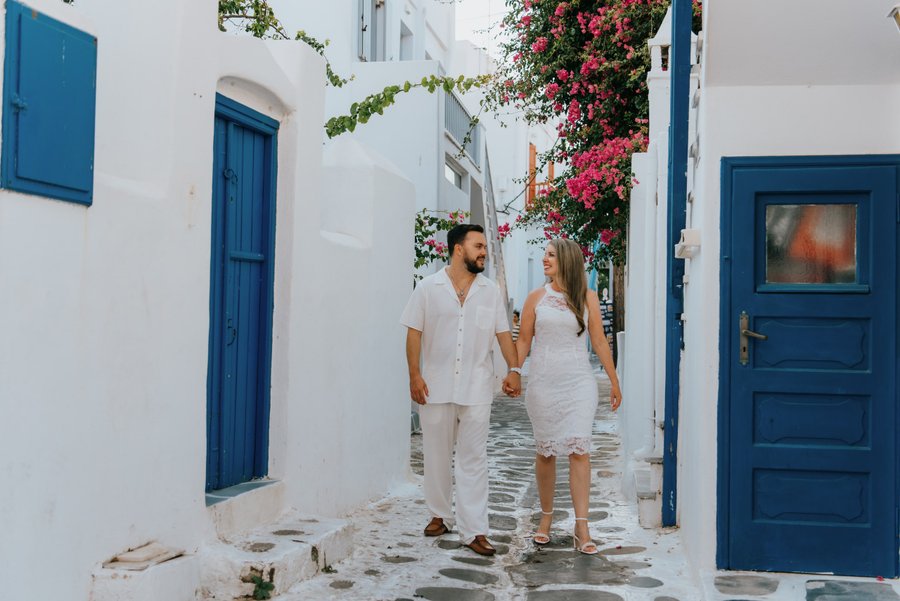 couple walking hand in hand through whitewashed alley with blue doors and pink bougainvillea in mykonos