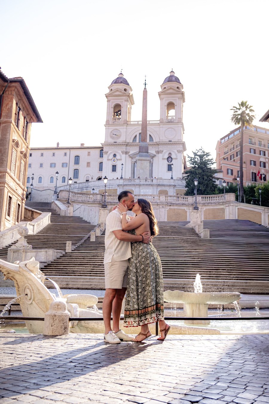 Couple kissing at the Spanish Steps in Rome with the obelisk and church facade in soft daylight