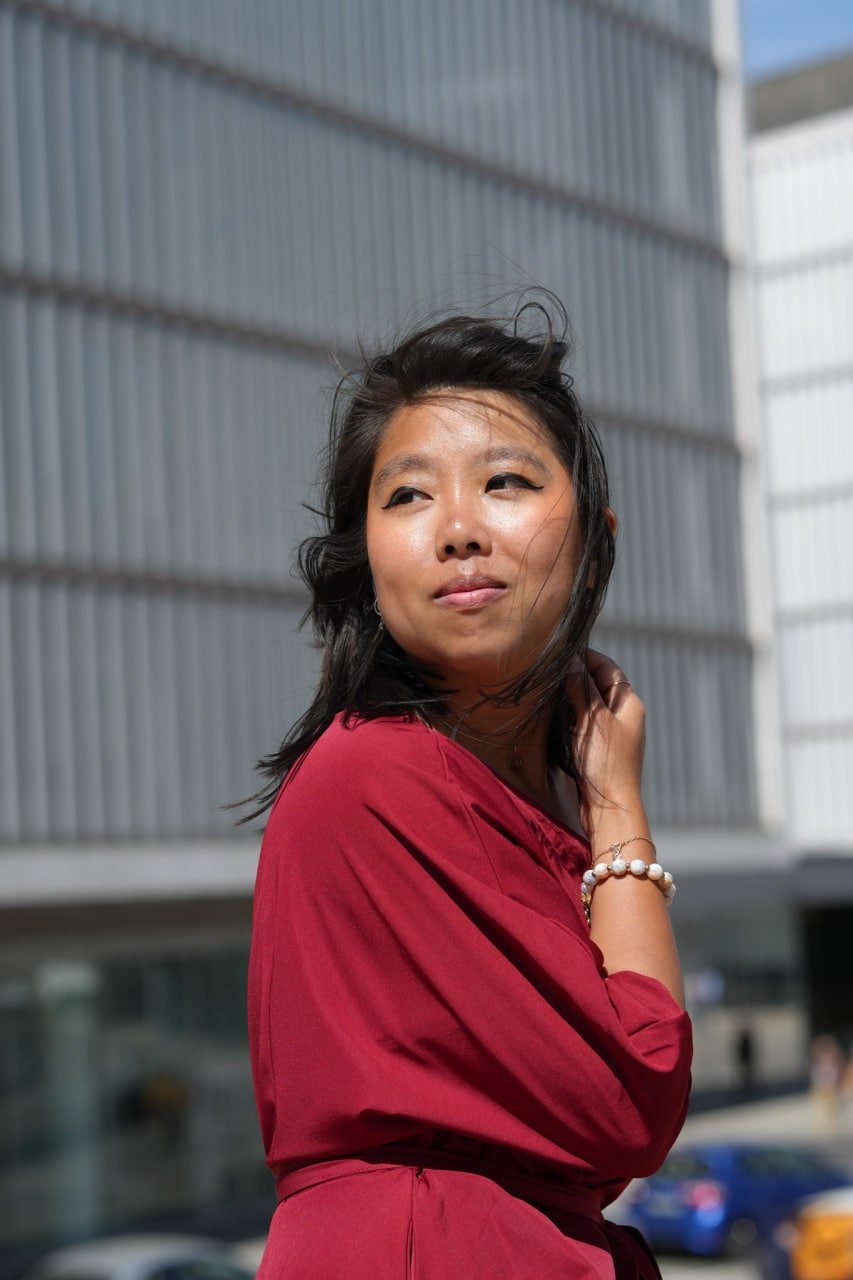 Solo traveler in red dress posing at modern architecture, bright daylight