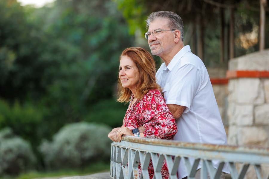 Mature couple standing on a stone balcony overlooking lush green surroundings in soft daylight