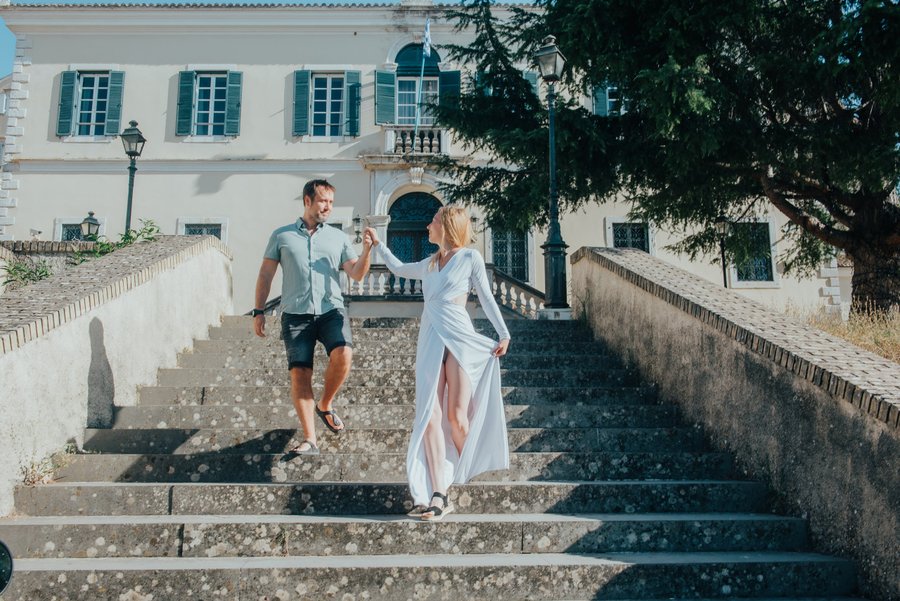 Couple walking down stone steps past a white neoclassical building in sunny Corfu old town