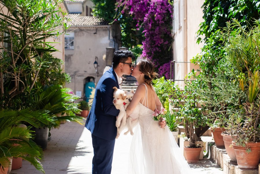 Couple kissing in a narrow alleyway surrounded by blooming bougainvillea and potted plants in Cannes